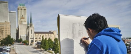 Artist drawing buildings with a pencil outside