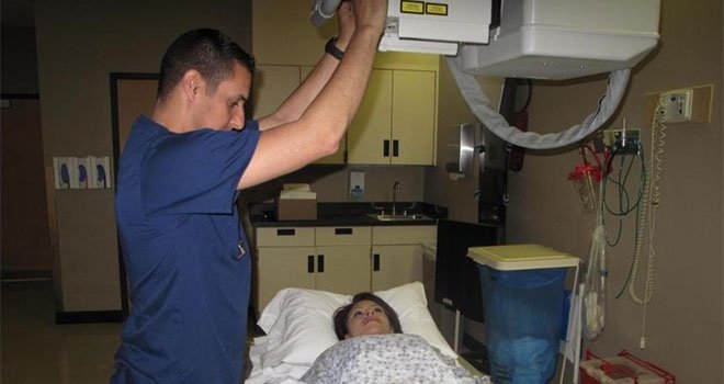 TCC Radiography student positions x-ray machine above a patient who is lying down.