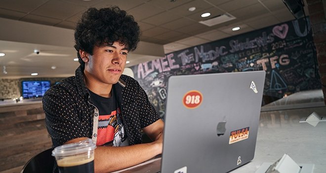 TCC Student works at his laptop in a coffee shop.
