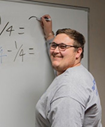 TCC Transfer Student Zach Little stands at a whiteboard teaching math.