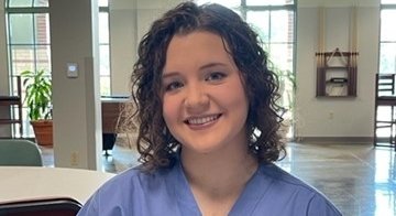 TCC Vet Tech Student sits at a table wearing blue scrubs
