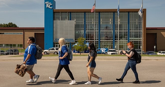 Four TCC True Blue Lead Students walk across the parking lot in front of southeast campus building.