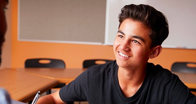 Young male high school student smiles while sitting in a classroom.