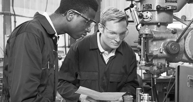 Two young men work at a machine in a manufacturing plant.