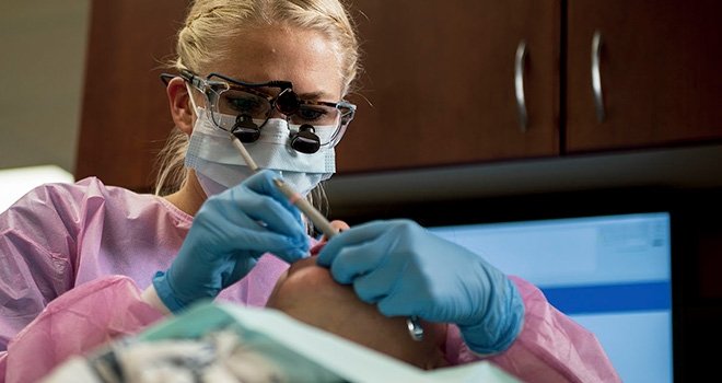 TCC Dental Hygiene student Wears magnification glasses and works diligently on a patient's teeth.