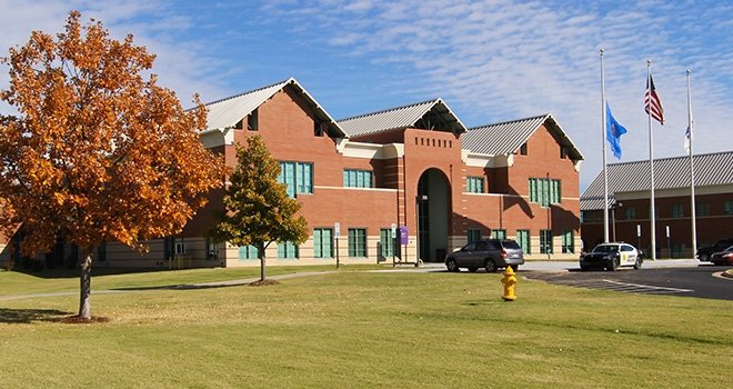 Entrance of TCC West Campus. Tree with orange leaves in the foreground. Oklahoma and American flags fly on flag poles.