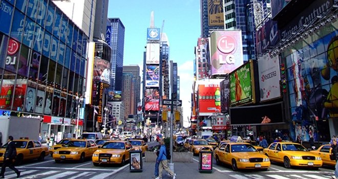 Street view of New Yorkers crossing the street in front of rows of yellow taxis at Time Square in New York City.