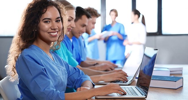 smiling nursing student with a laptop and other students in the background