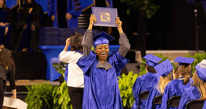 TCC Graduate in cap and gown hold diploma cover over her head.