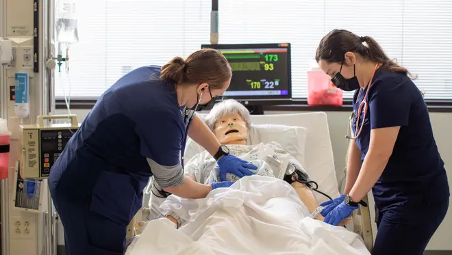 Two students work over a nursing manikin