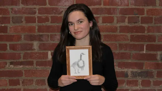 Sophia Freudenberger holds up her drawing that won the holiday card contest. It is a small, pencil drawing of a Canada goos with a wreath around its neck.