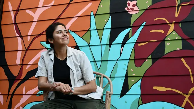 Zadith Rodriguez sits in front of a brightly colored mural