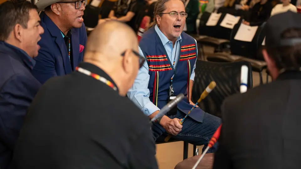 Five men are sitting and performing in a drum circle.