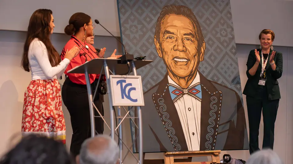 Four students stand beside a 6-foot-by-5-foot spray-painted portrait of Wes Studi.
