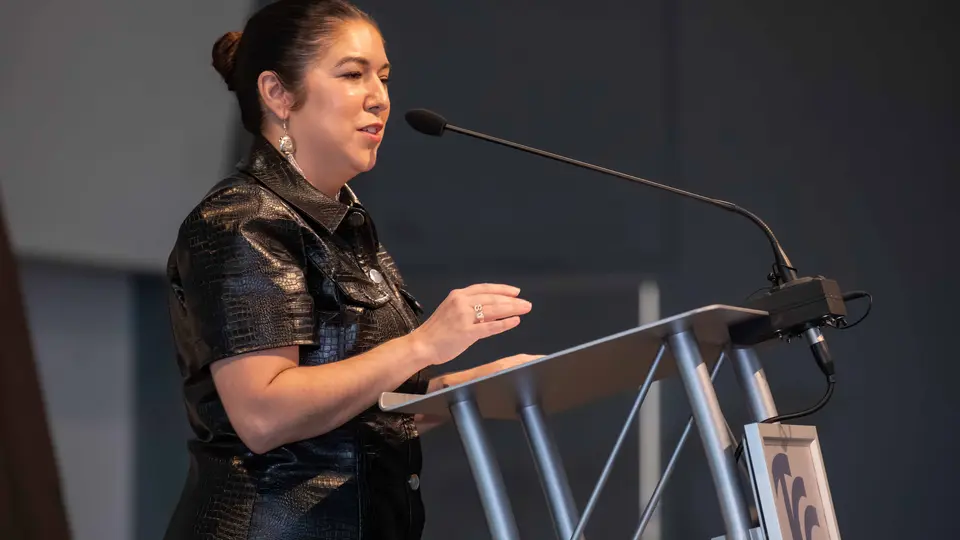 Amanda Swope stands a podium and speaks into a microphone. She wears a black dress.