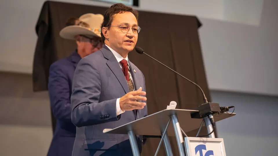 Chief Chuck Hoskin stands at a podium and is speaking. He wears a gray suit jacket with a red tie.
