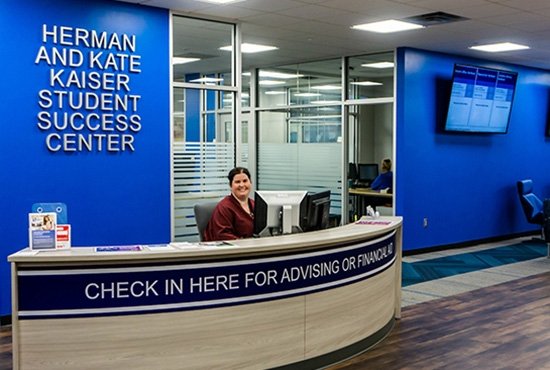 TCC employee smiles as they sit at the reception counter of TCC Herman & Kate Kaiser Student Success Center.