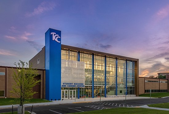 Lights illuminate the two-story glass windows of the TCC Southeast Campus Students Success Center as the sun sets to the right.