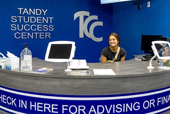 TCC employee smiles as they sit at the reception counter of TCC A.R. & Marylouise Tandy Student Success Center.