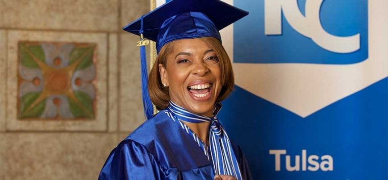 Smiling black woman wears her TCC graduation cap and gown.