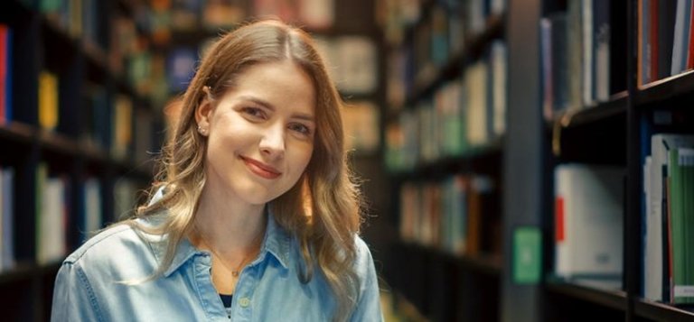 TCC female student stands in front of library book shelves