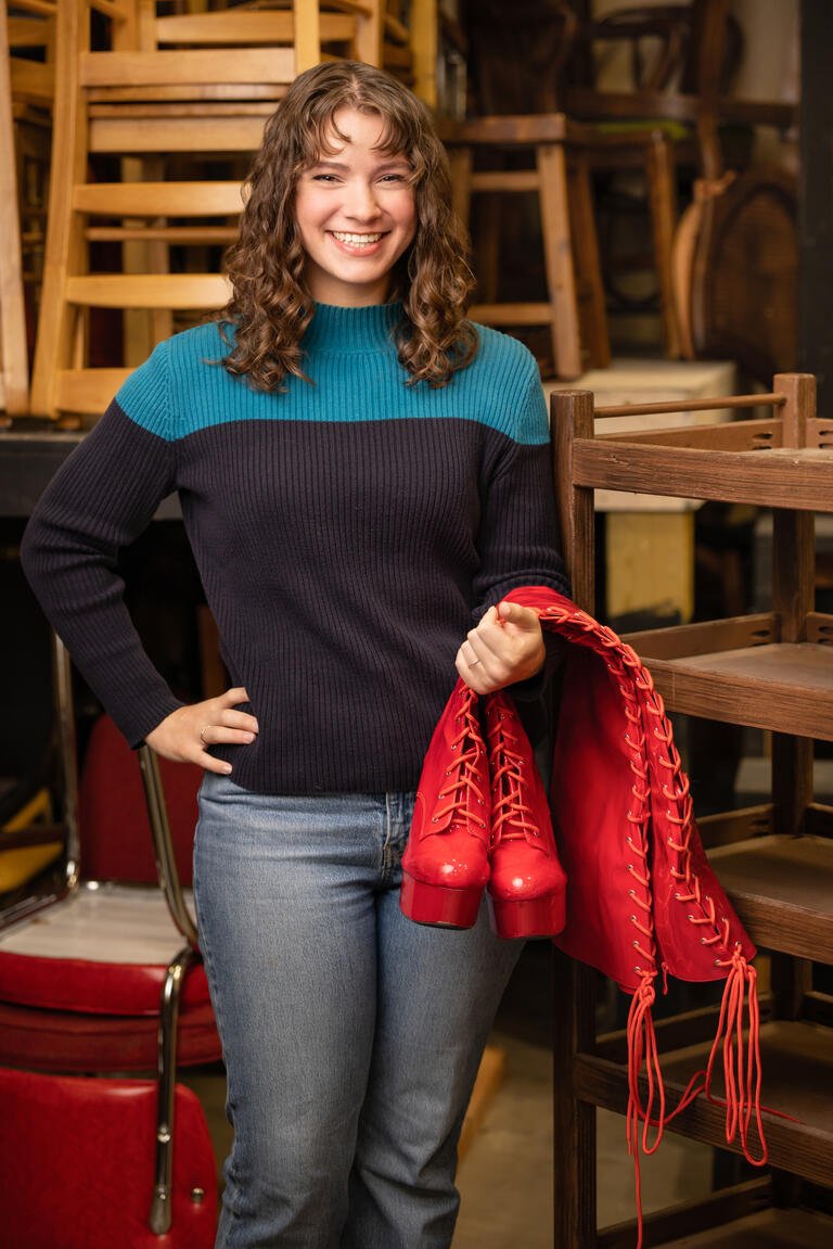 Moriah Jestus smiles with tall, red boots draped over her left arm.